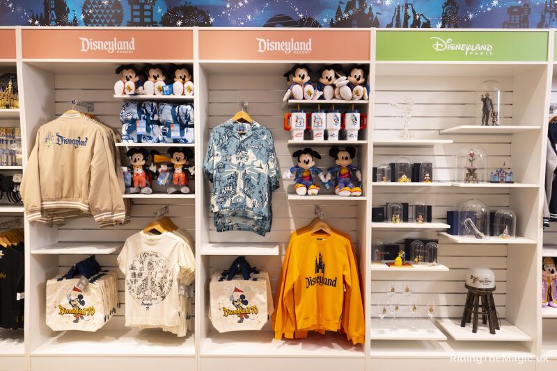 clothing hanging in white inlets with soft toys on shelves different coloured signs above peach with words Disneyland and green with Disneyland Paris