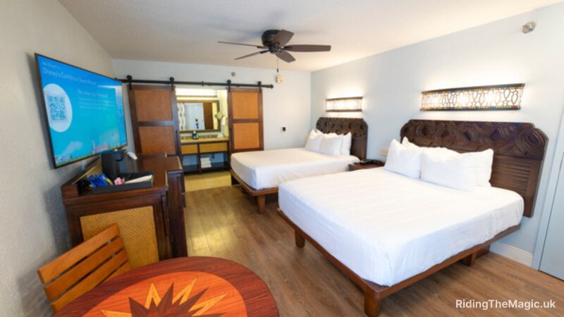 A hotel room with two beds, a table, a television, and a ceiling fan