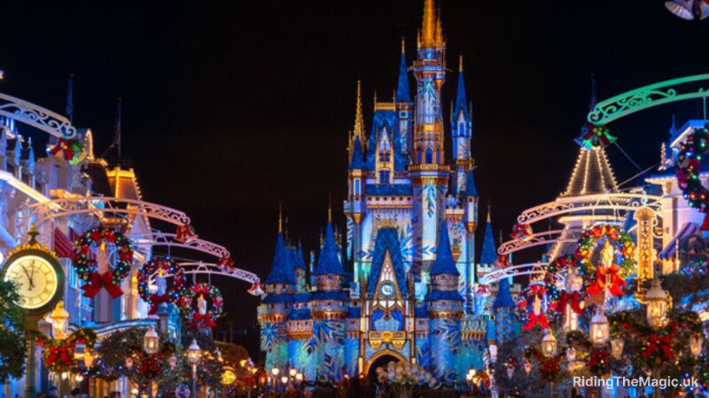 Cinderella castle with blue snow flake Christmas overlay, Christmas wreaths with multicoured baubleshanging above lights festive scene