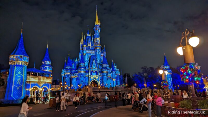 People are walking around the blue lit Cinderella Castle at night