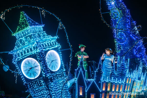 boy in green suit with hat girl in blue dress with blue bow in hair lights all over big ben and top of buildings float parade disney starlight night time show