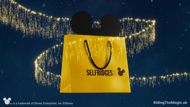 Yellow shopping bag with black handle and black Mickey Mouse ears coming out of the top. Writing in botoom of thirs of yellow bag is black: Selfridges with black mickey mouse emoji Blue starlight background with zig zag of gold glitter shooting through background