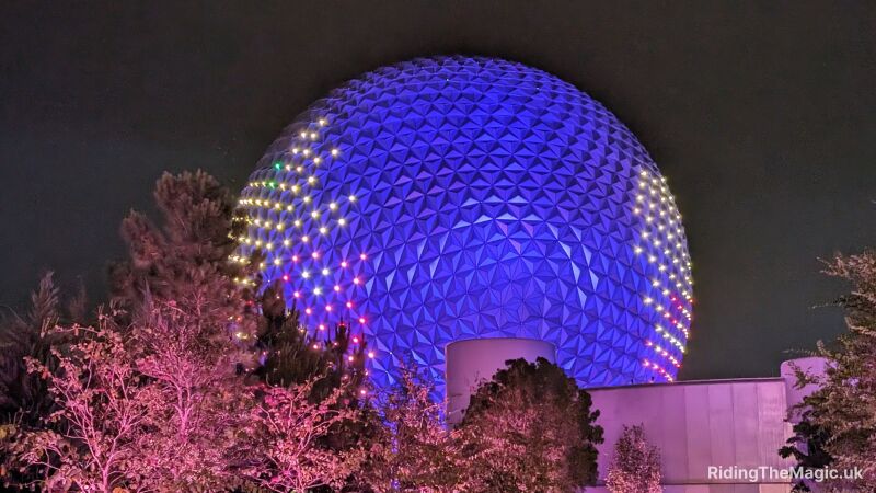 Epcot's Spaceship Earth at night with purple lights and trees in the foreground