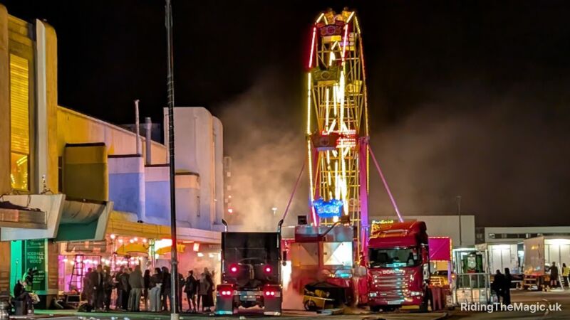 night sky smoke in air 2 US style trucks, a ferris wheel, and people standing by lamp post