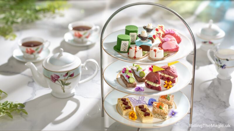 A three-tiered tea stand with teacups, teapots, and a variety of desserts