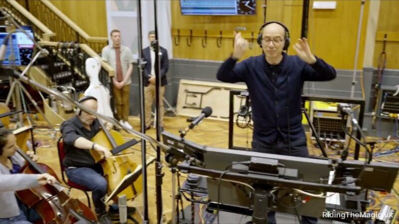 A man is conducting a band while wearing headphones in a recording studio
