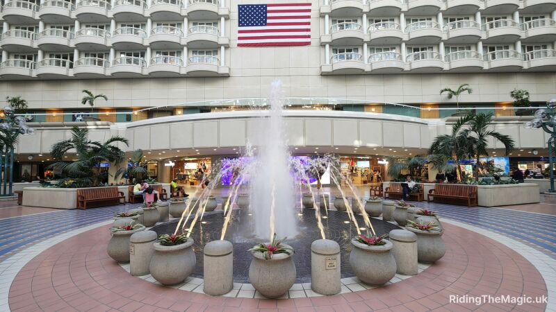 fountain with pots around, tiled floor, american flag on white wall orlando airport