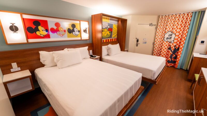 Two twin beds in a Disney hotel room with Mickey Mouse artwork on the walls
