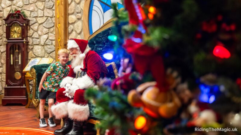 Santa Claus sits on a chair with a child, near a Christmas tree