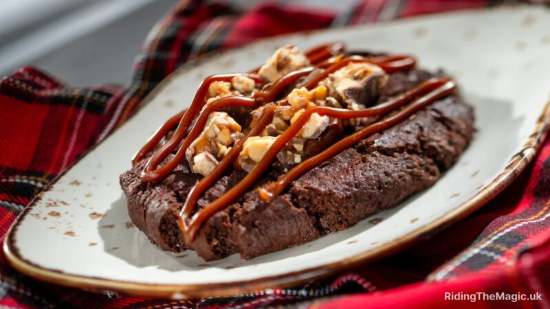 A chocolate cookie with caramel and nuts on a white plate with a red cloth