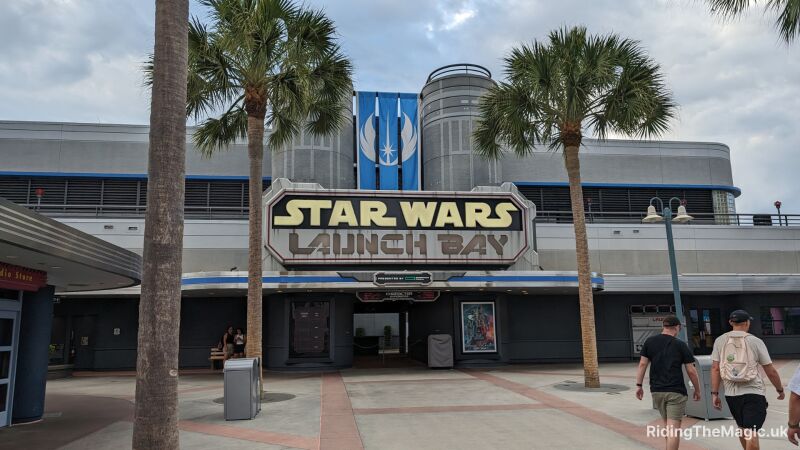 path with two palm trees and building behing with sign saying star wars launch bay three oblong blue flags above