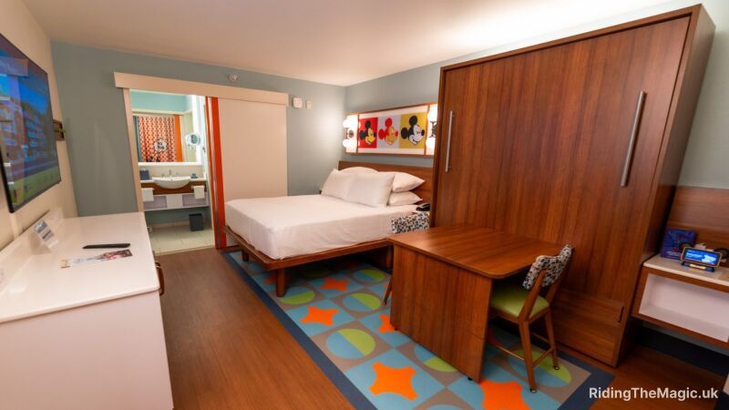 A Disney hotel room with a bed, desk, and a colorful rug