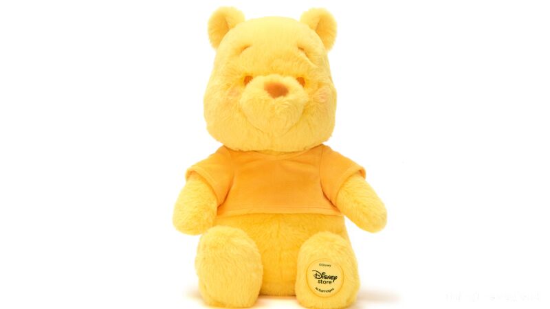 Winnie the Pooh plush sitting on a white background wearing a yellow shirt