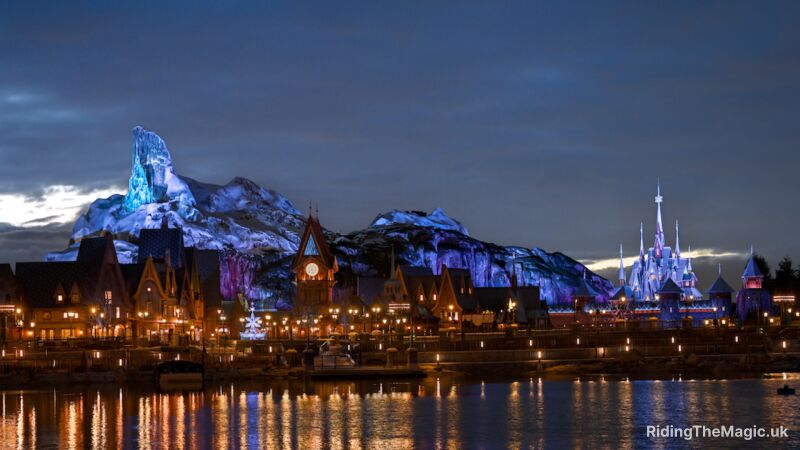 Night view of a Disney park with a castle and mountains in the background