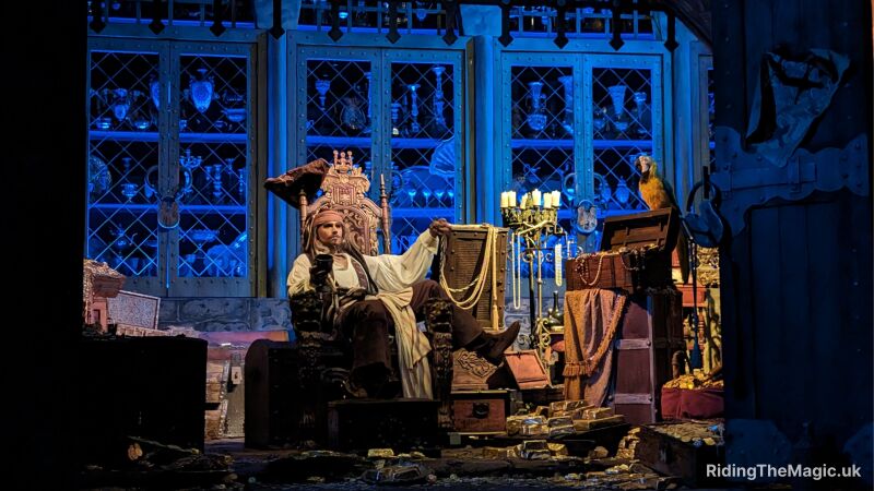 Captain Jack Sparrow sitting in a chair drinking surrounded by treasures