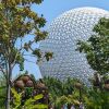 A large geodesic dome rises above lush tropical landscaping and trees under a clear blue sky.