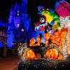 Nighttime parade float with a colorful dragon and a skeleton musician glowing in orange and blue lights in front of a lit castle.