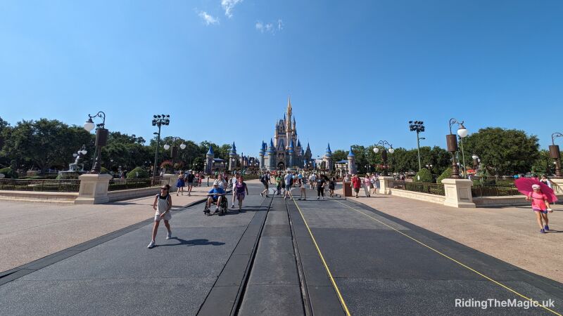 Visitors stroll down Main Street toward Cinderella Castle at Magic Kingdom under a clear blue sky.