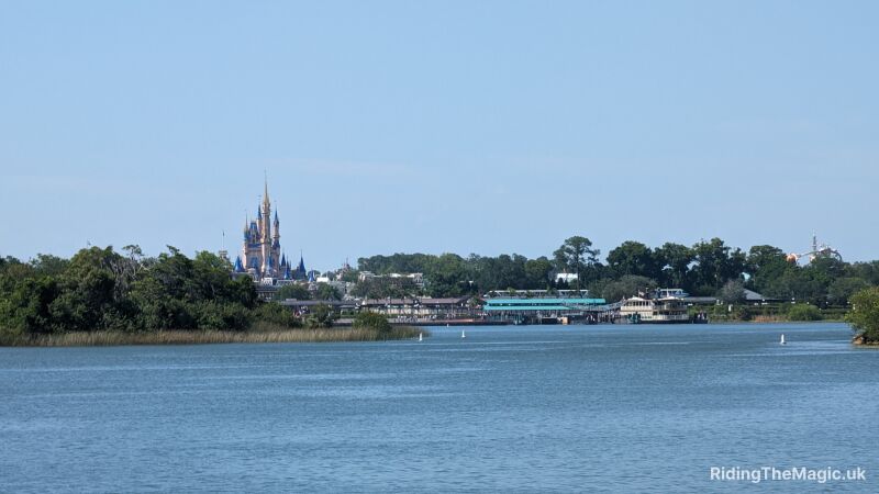 Lake in the foreground with a distant fairy-tale castle and shoreline buildings beneath a clear blue sky.