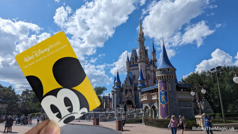 Hand holding a yellow Walt Disney World card featuring Mickey Mouse in front of Cinderella Castle under a blue sky.